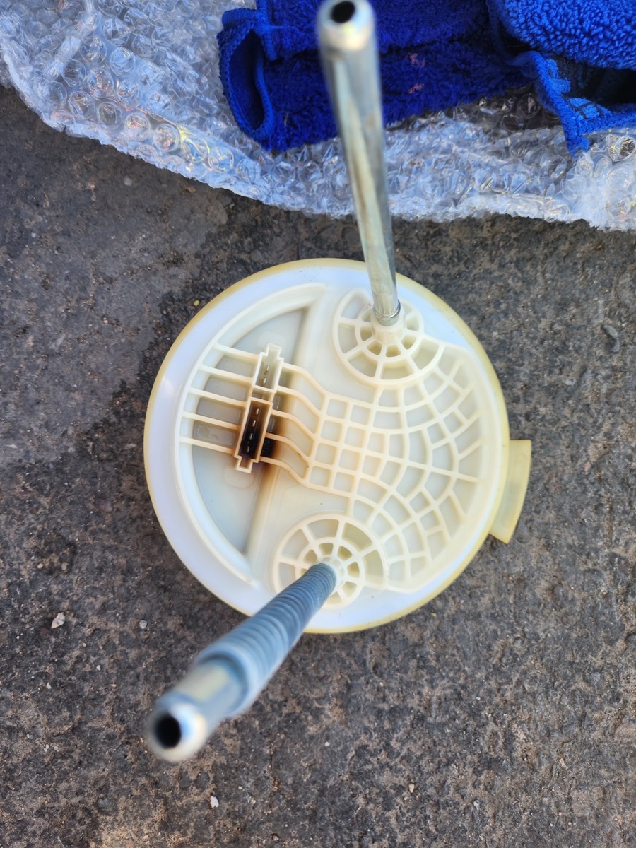 A fuel pump assembly pulled from a car and laid on the pavement
